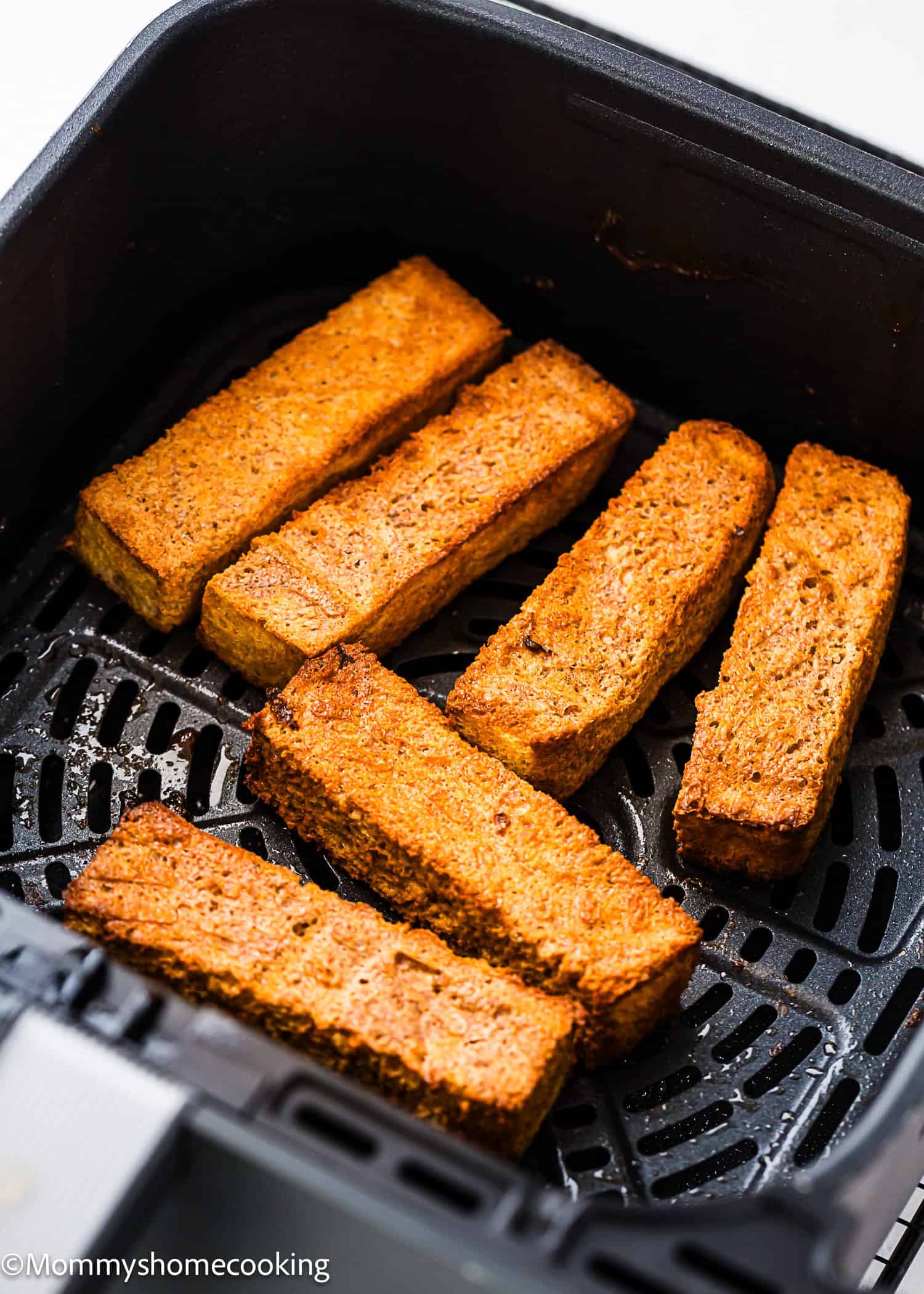 Six golden-brown Air Fryer Eggless French Toasts arranged in an air fryer basket.
