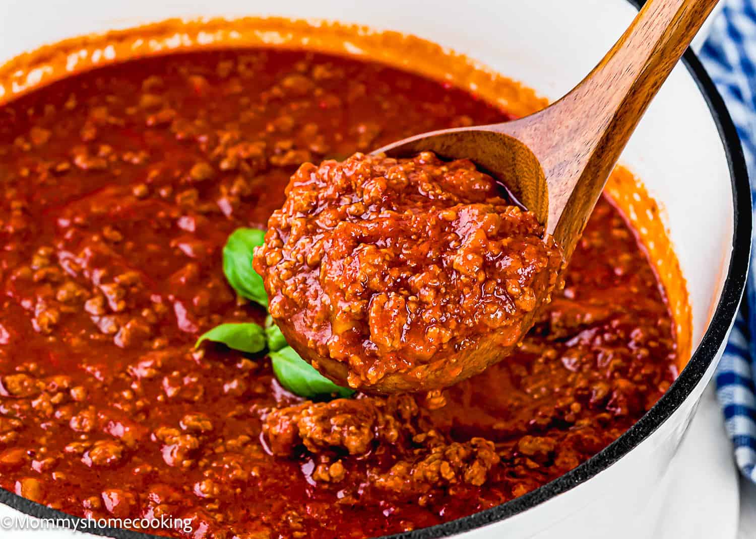 A wooden spoon scoops up thick, chunky Classic Italian Bolognese Sauce from a pot filled with rich red tomato-based sauce.