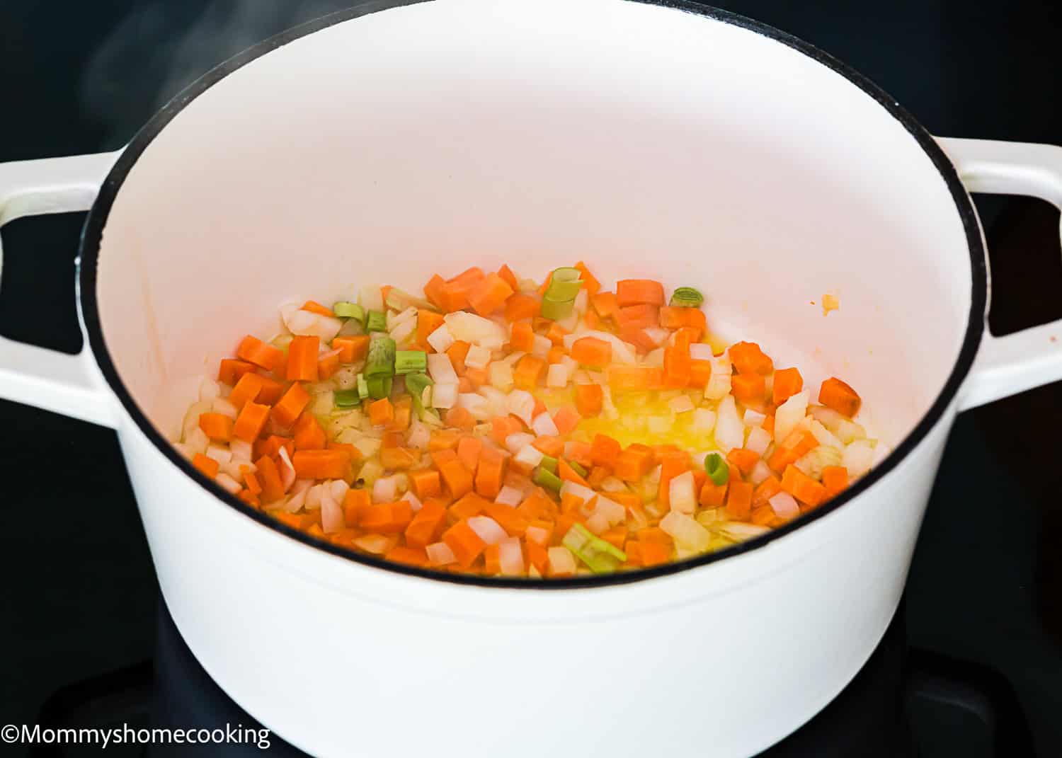 Diced carrots, celery, and onions are sautéing in a white pot on the stovetop, forming the flavorful base for a Classic Italian Bolognese Sauce.
