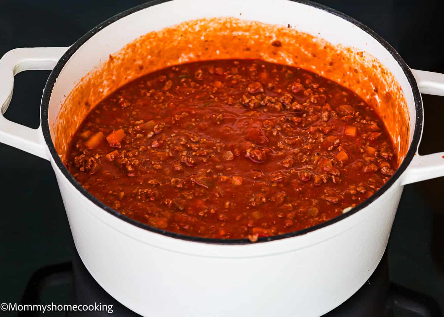 A white pot filled with simmering ground beef and tomato sauce, creating a Classic Italian Bolognese Sauce, sits on a stovetop.
