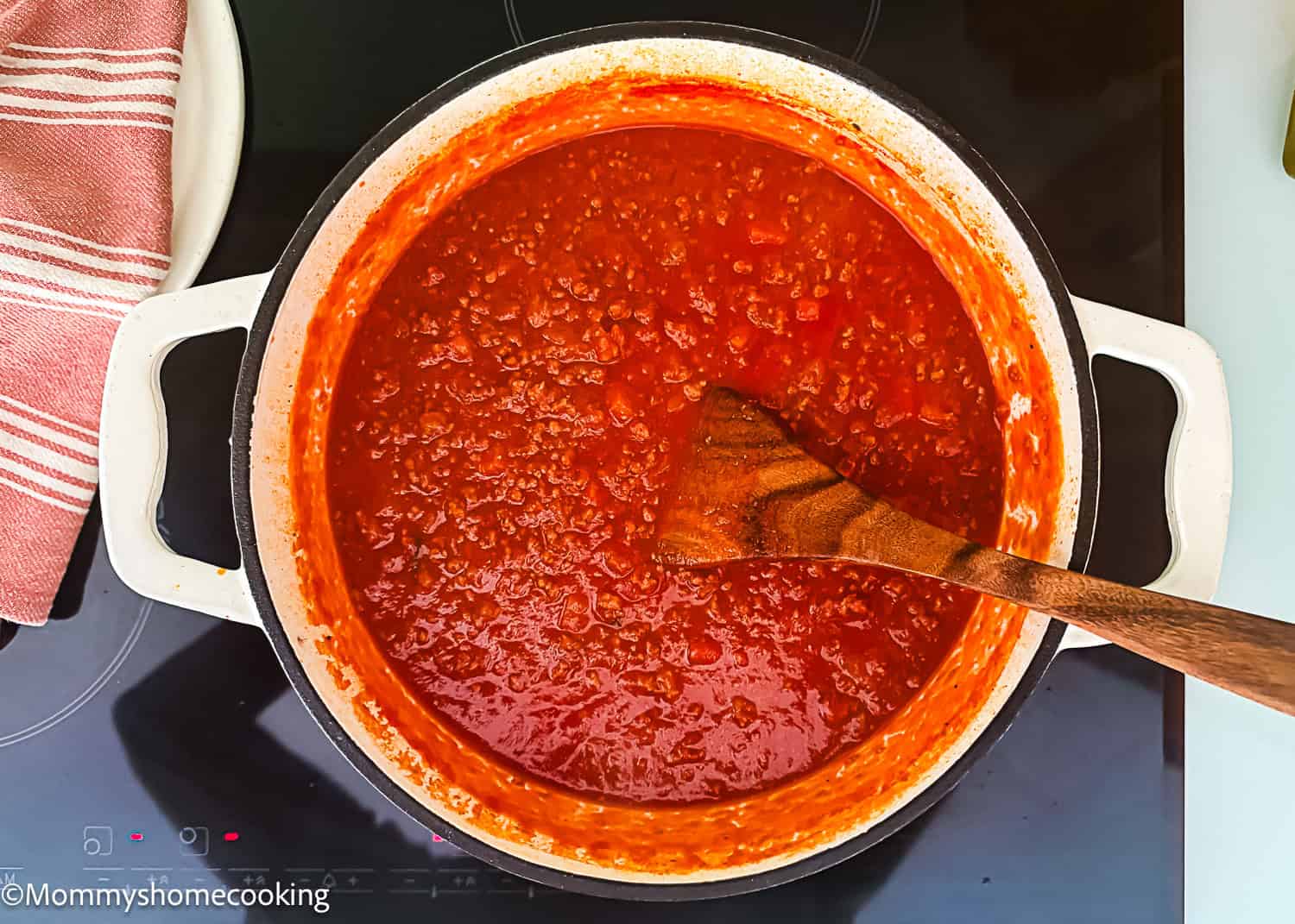 A pot of Classic Italian Bolognese Sauce with ground meat is being stirred with a wooden spoon on a stovetop.