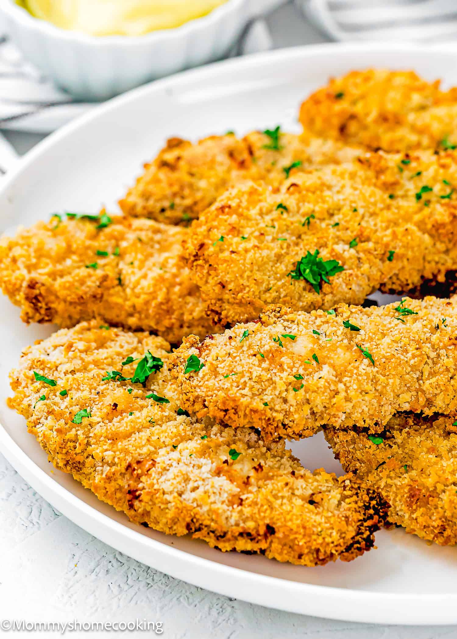 A white plate features several golden-brown Easy Air Fryer Chicken Tenders (No Eggs - No Dairy) garnished with chopped parsley.