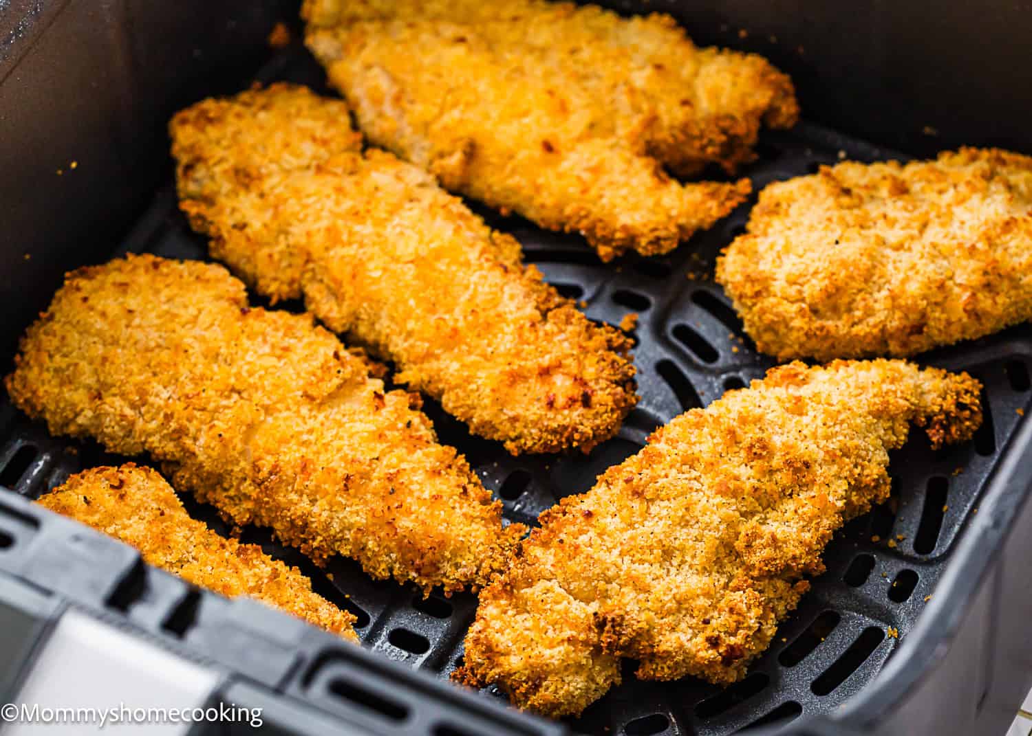 Six breaded chicken tenders are arranged inside an air fryer basket, cooked to a golden brown for an easy Air Fryer Chicken Tender (No Eggs - No Dairy) option.
