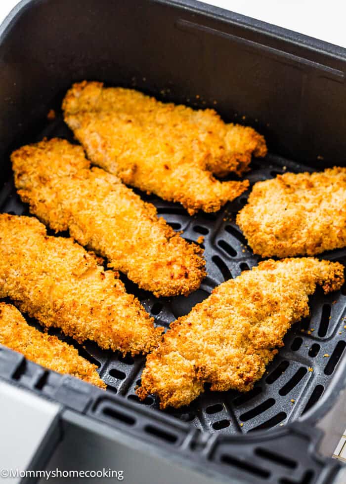 Six Easy Air Fryer Chicken Tenders (No Eggs - No Dairy) are arranged in a black air fryer basket, cooked to a golden brown.