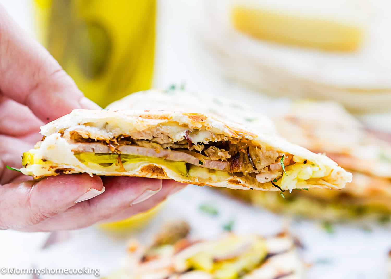 A hand holds a sliced empanada revealing layers of meat, eggs, and pastry filling—perfect alongside Easy Cuban Quesadillas.