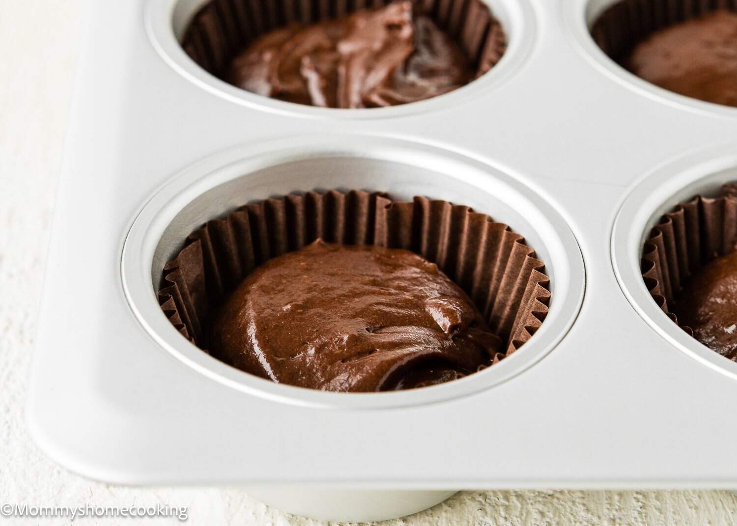 A close-up of Eggless Chocolate Cream Cupcakes (hostess cupcakes) batter in brown paper liners placed in a metal muffin tin, ready to be baked.