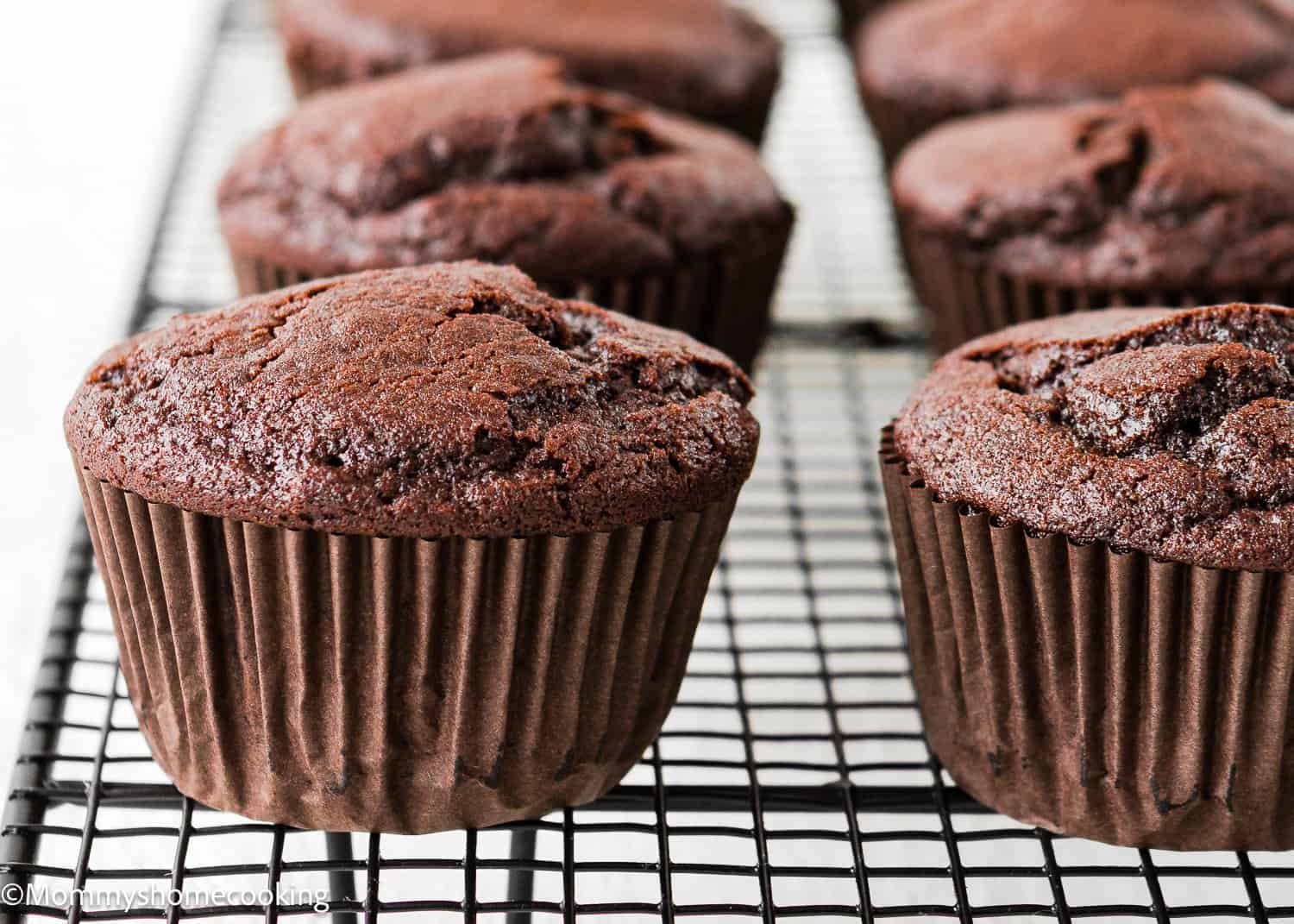 Eggless Chocolate Cream Cupcakes (hostess cupcakes) in brown paper liners are cooling on a black wire rack.
