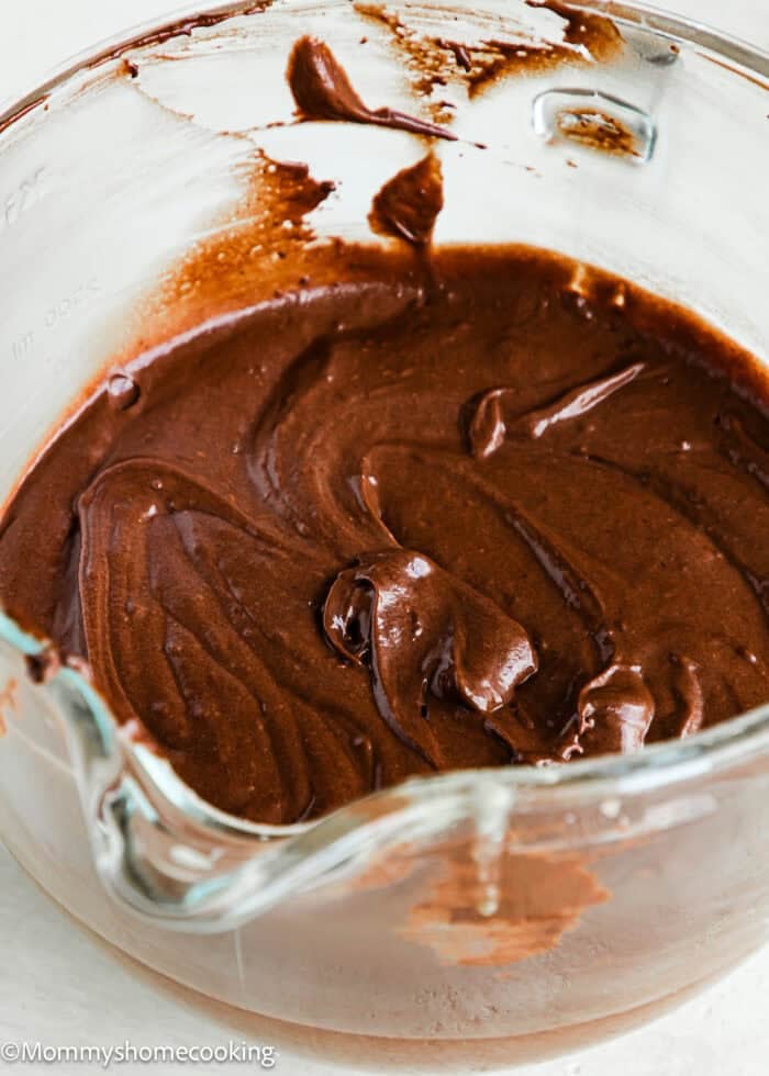 A glass mixing bowl filled with smooth, swirled Eggless German Chocolate Sheet Cake batter.