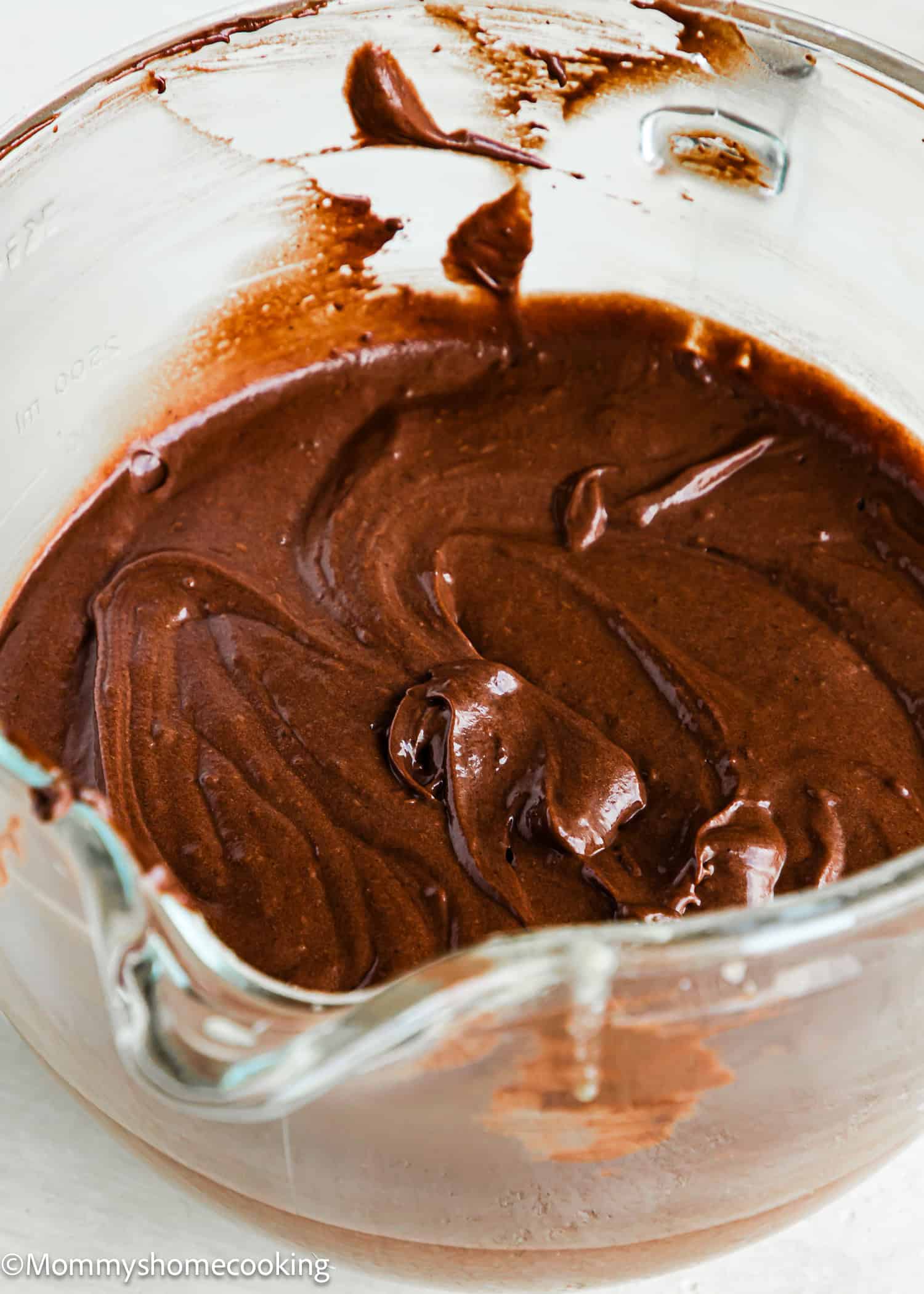 A glass mixing bowl filled with smooth, swirled Eggless German Chocolate Sheet Cake batter.