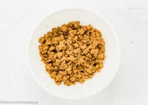 A white bowl filled with cooked, seasoned ground meat sits on a white surface, perfect to pair with a slice of Eggless Peach Coffee Cake.