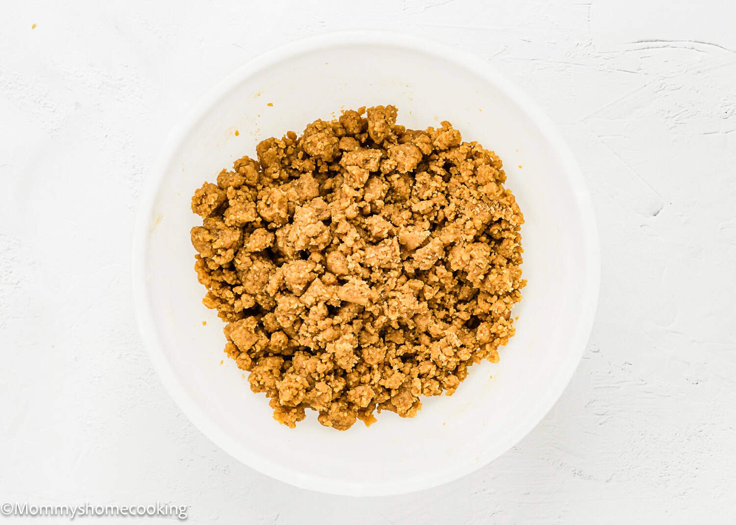 A white bowl filled with crumb mixture, perfect to top an Eggless Peach Coffee Cake.