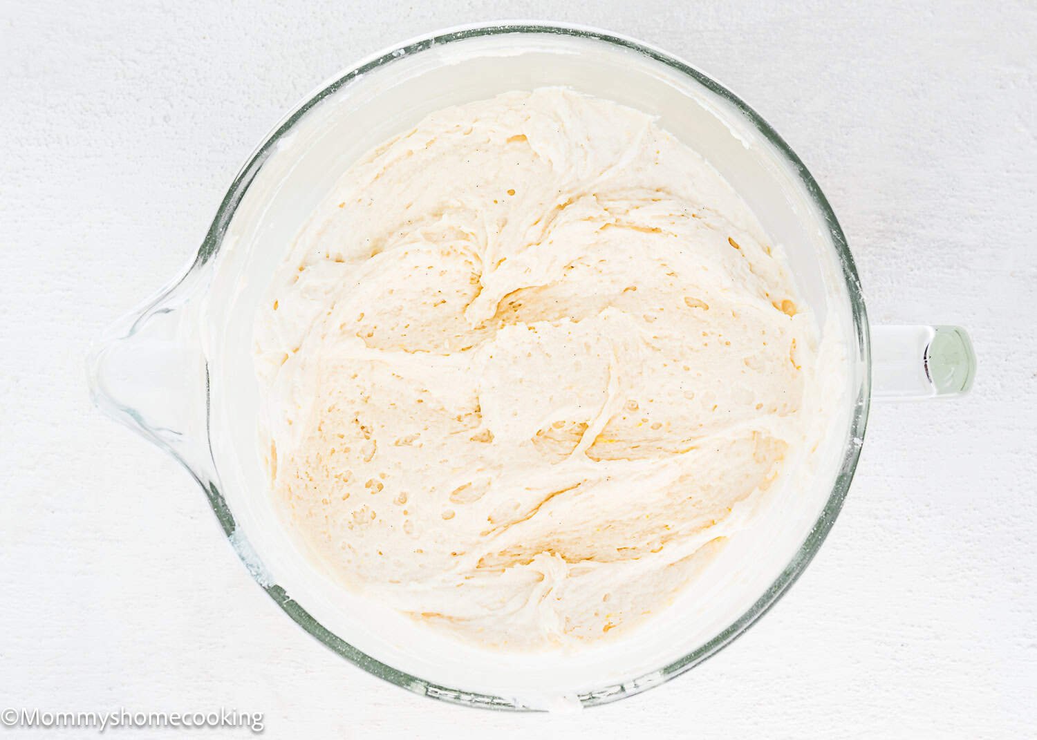 A glass mixing bowl filled with risen bread dough sits on a white surface, ready to inspire Eggless White Chocolate Raspberry Cupcakes.