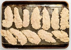 Homemade Chicken Tenders (Egg & Dairy-Free) are arranged in rows on a wire rack over a baking sheet, ready to be baked.