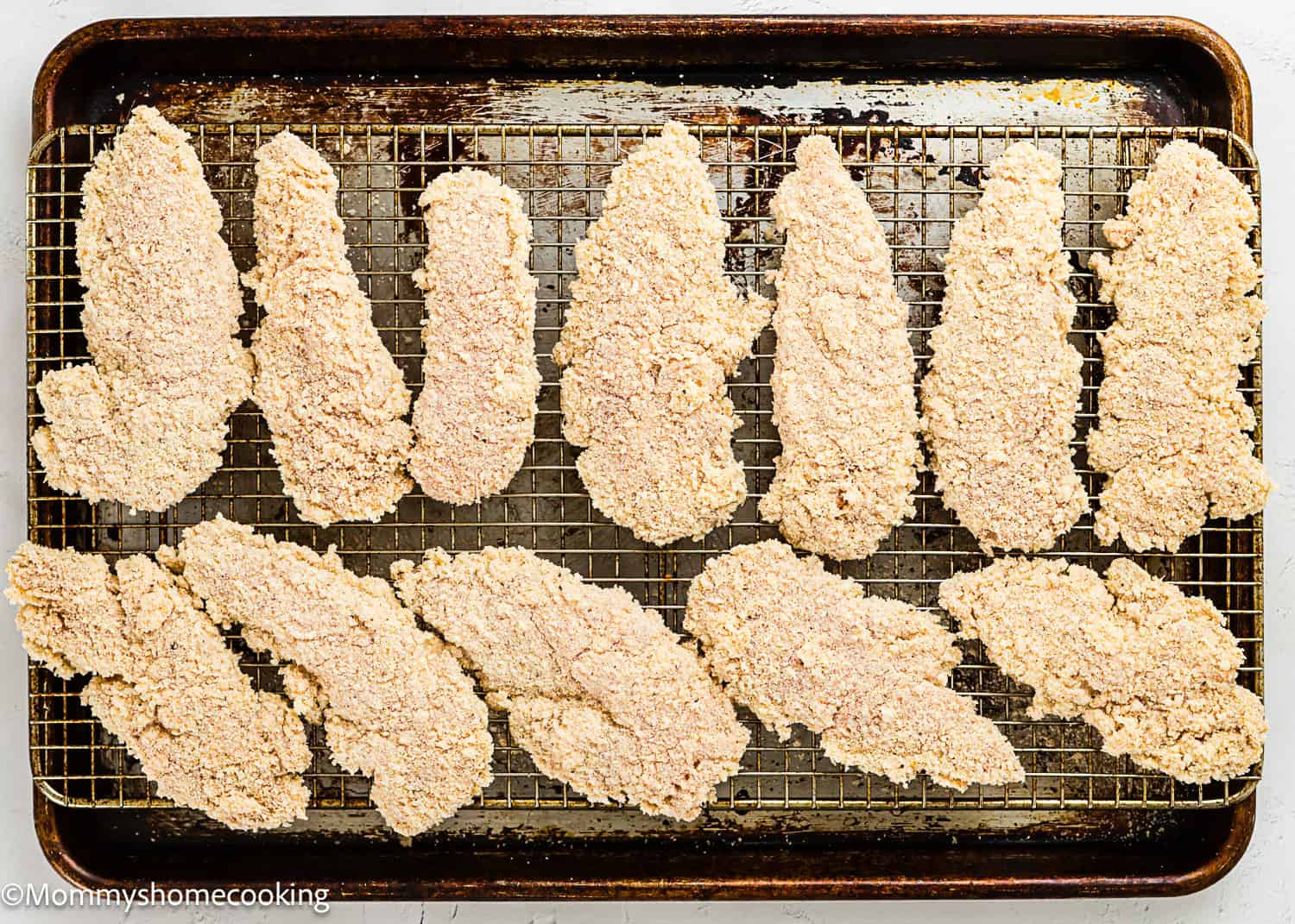 Homemade Chicken Tenders (Egg & Dairy-Free) are arranged in rows on a wire rack over a baking sheet, ready to be baked.