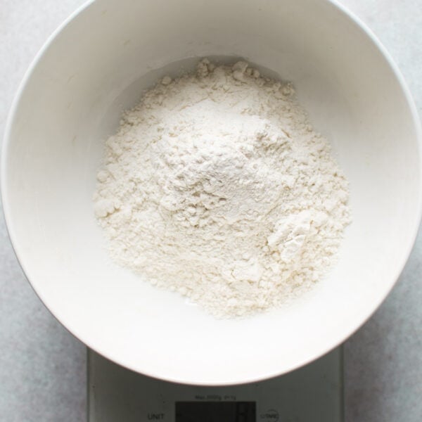 A white bowl filled with flour is placed on a digital kitchen scale, showing a key step in How-to-make-my-recipes-gluten-free by measuring alternative flours accurately.