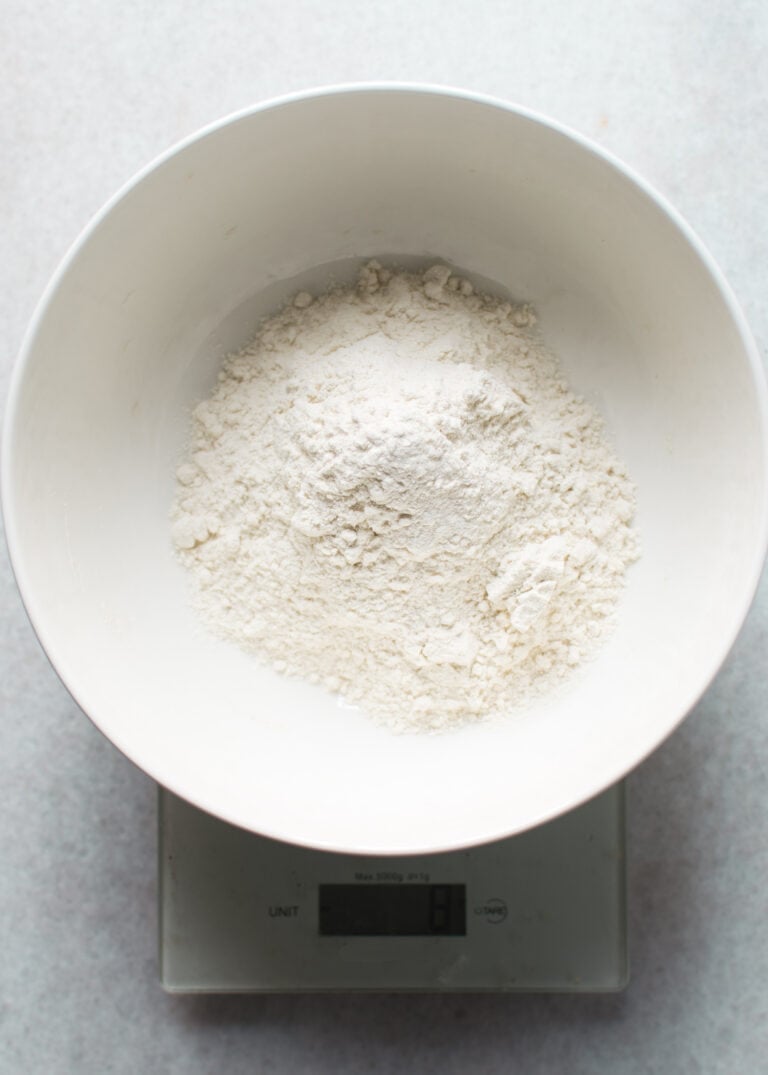 A white bowl filled with flour is placed on a digital kitchen scale, showing a key step in How-to-make-my-recipes-gluten-free by measuring alternative flours accurately.