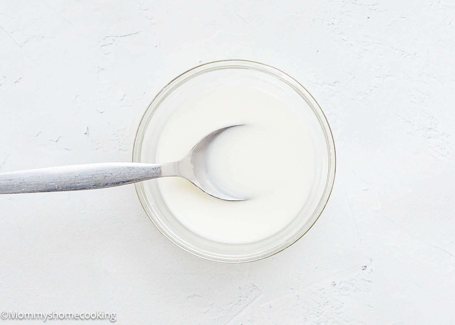 A glass bowl filled with cornstarch slurry with a metal spoon resting inside on a white surface—perfect for pairing with Raspberry Dessert Sauce Recipe.