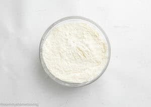 A glass bowl filled with white powdered flour on a light-colored surface, perfect for baking a soft, fluffy Egg-Free Vanilla Cake without eggs.