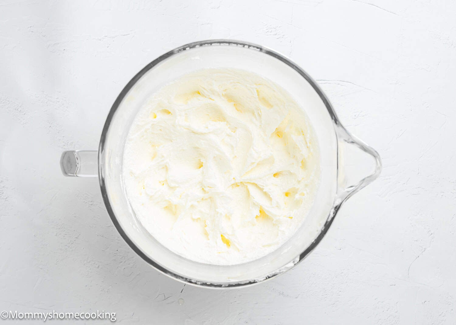A glass mixing bowl filled with creamed butter and sugar sits on a white surface, perfect for egg-free vanilla cake—a soft, fluffy birthday cake without eggs.