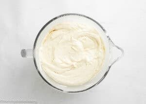 A glass mixing bowl filled with smooth, creamy egg-free vanilla cake batter—perfect for a soft, fluffy birthday cake without eggs—on a white surface.