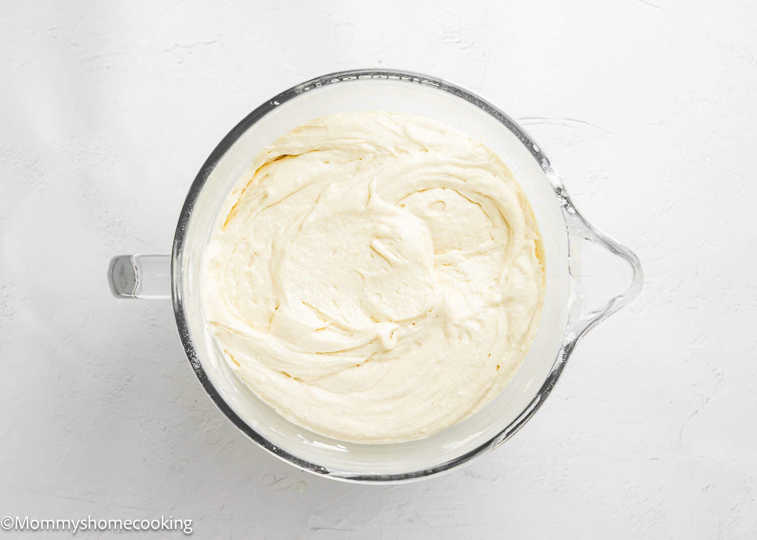 A glass mixing bowl filled with smooth, creamy egg-free vanilla cake batter—perfect for a soft, fluffy birthday cake without eggs—on a white surface.