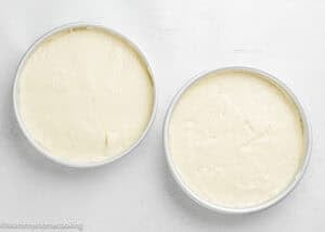 Two round cake pans filled with smooth, unbaked Egg-Free Vanilla Cake – soft and fluffy birthday cake without eggs rest on a light-colored surface.