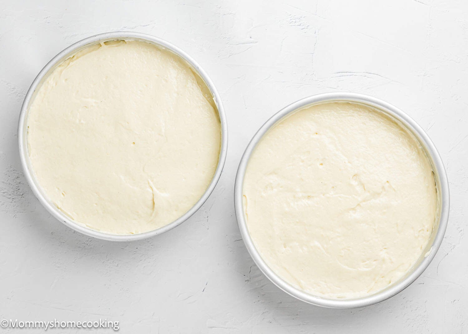 Two round cake pans filled with smooth, unbaked Egg-Free Vanilla Cake – soft and fluffy birthday cake without eggs rest on a light-colored surface.