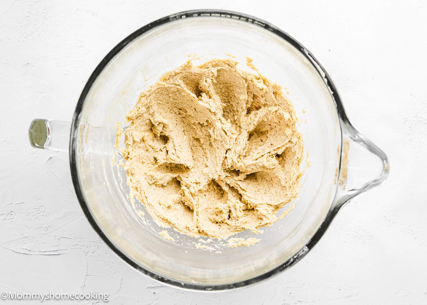 A glass mixing bowl containing creamed dough for Eggless S’mores Cookie Bars sits on a white surface.