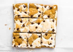 Nine rectangular Eggless S’mores Cookie Bars with toasted marshmallow, chocolate chips, and a cookie base, arranged in a 3x3 grid on white parchment paper.