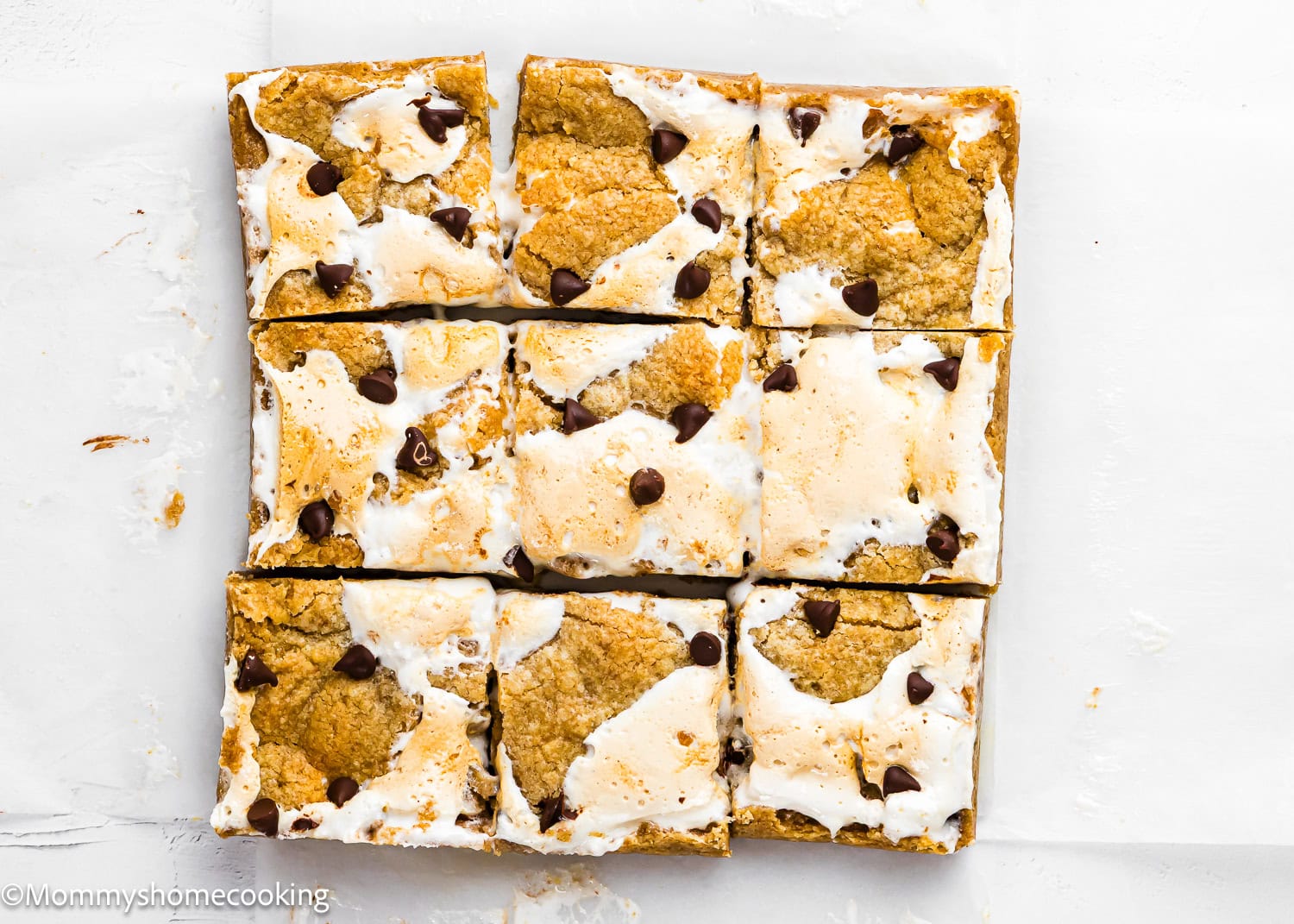 Nine rectangular Eggless S’mores Cookie Bars with toasted marshmallow, chocolate chips, and a cookie base, arranged in a 3x3 grid on white parchment paper.