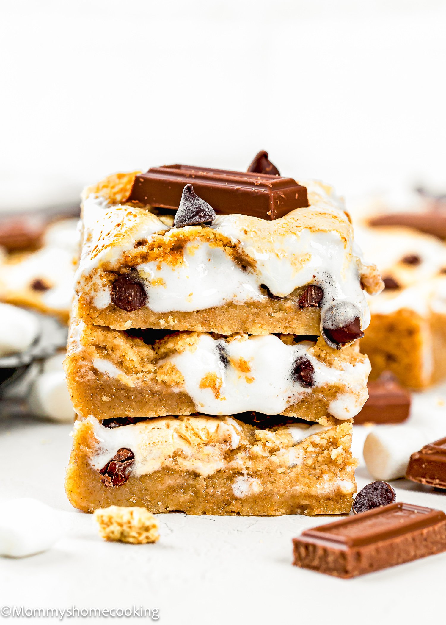 Three stacked Eggless S’mores Cookie Bars with visible chocolate chips, marshmallow, and chocolate pieces on top, set against a light background.