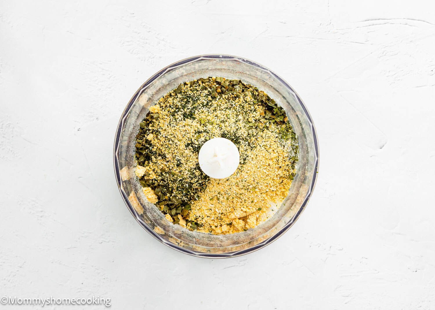 A food processor bowl filled with chopped herbs, breadcrumbs, and Homemade Ranch Seasoning Mix (Allergy-Friendly & Dairy-Free Option!), viewed from above on a white surface.