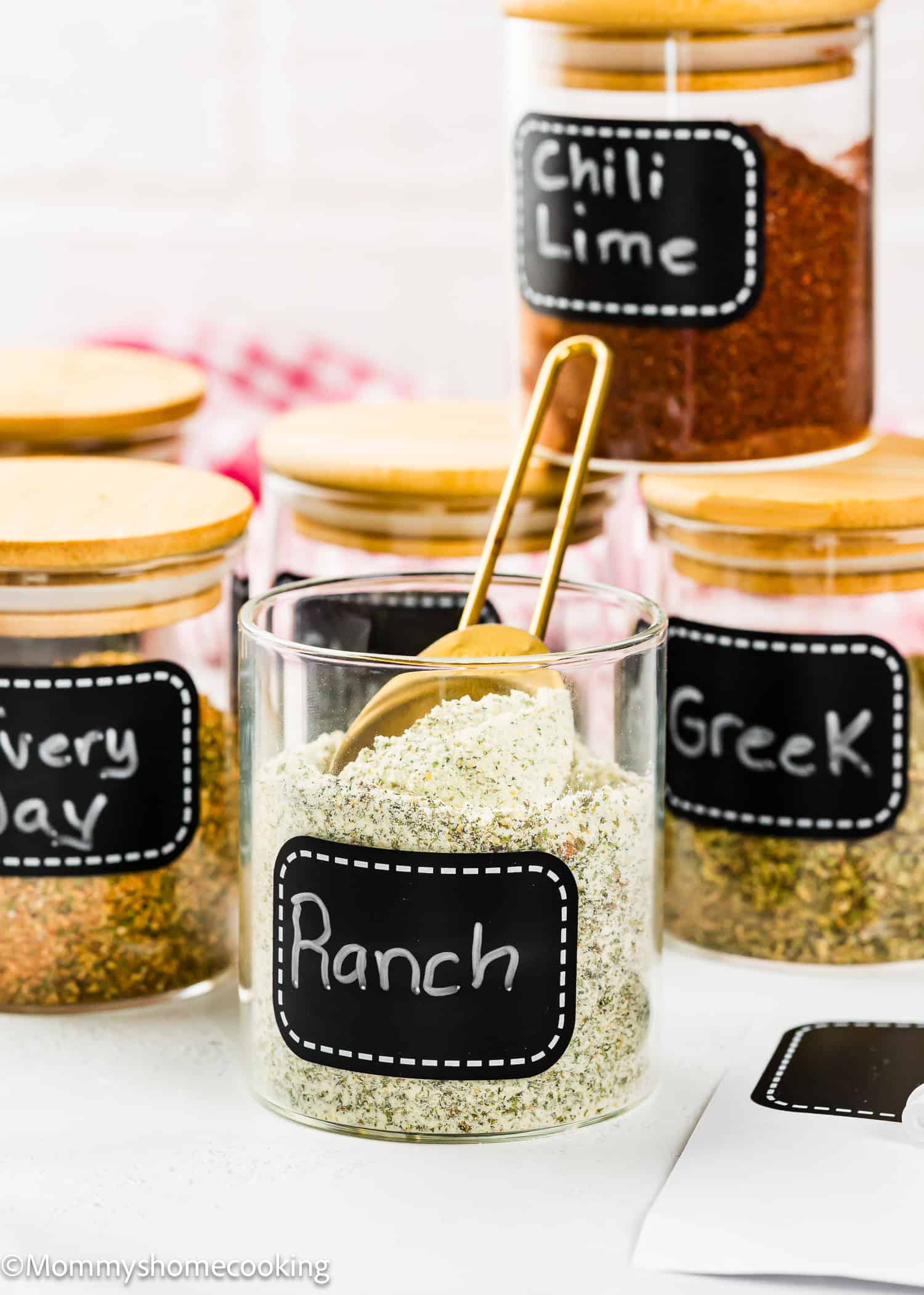 A glass jar labeled "Ranch" filled with Homemade Ranch Seasoning Mix (Allergy-Friendly & Dairy-Free Option!), and a gold measuring spoon, surrounded by similar jars labeled "Chili Lime," "Greek," and "Everyday.