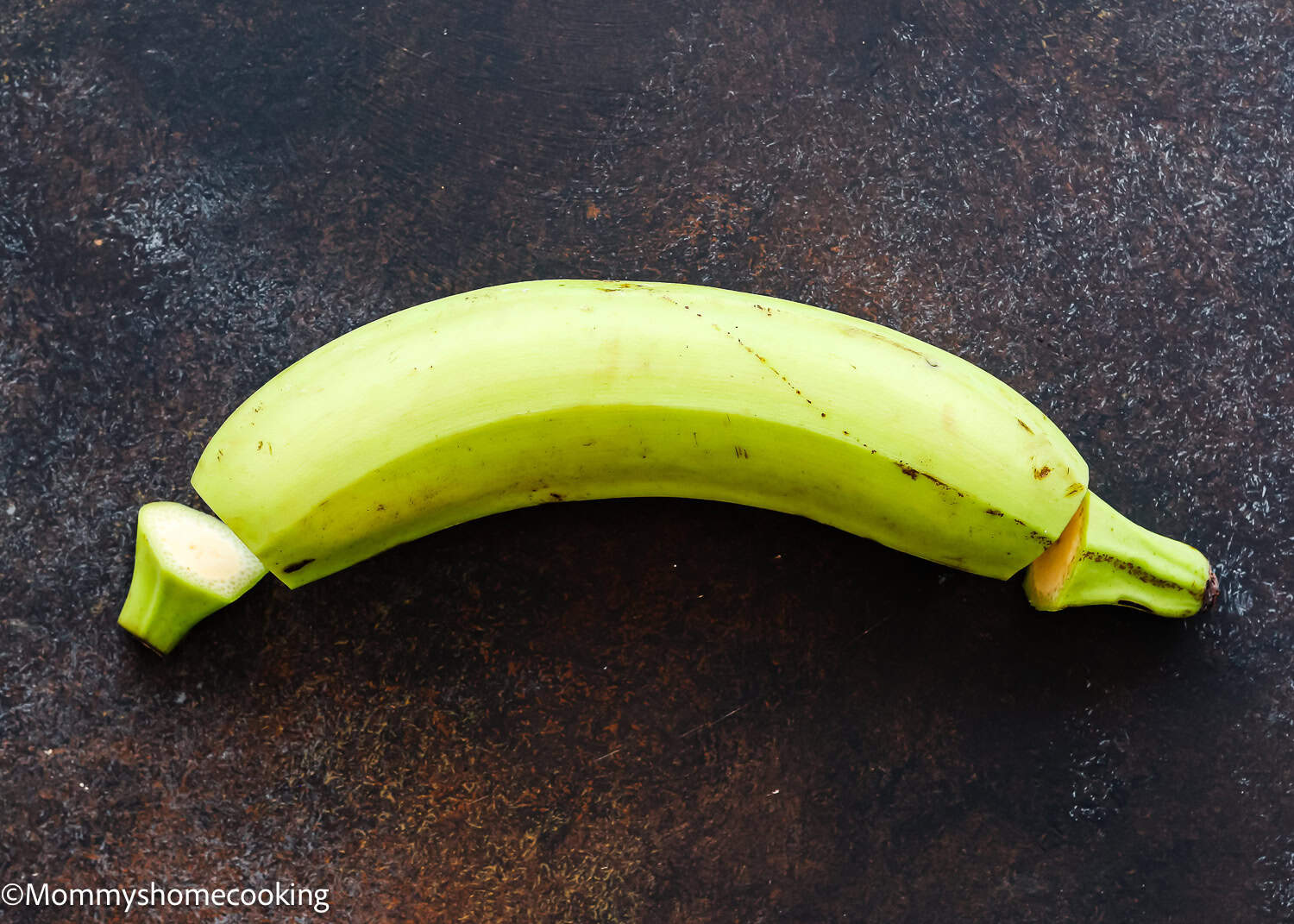 A whole green plantain with both ends cut off, placed on a dark textured surface—perfect for learning How to Make Tostones (Crispy Fried Green Plantains – Easy & Authentic!).