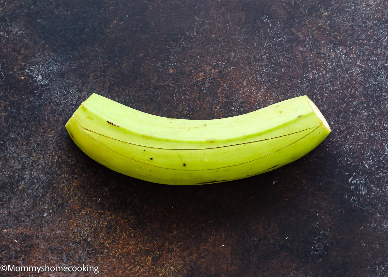 A whole, unpeeled green plantain rests on a dark, textured surface—perfect for learning How to Make Tostones (Crispy Fried Green Plantains – Easy & Authentic!).