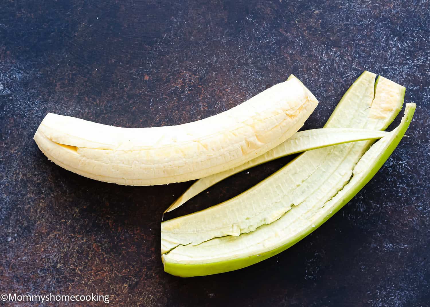A peeled green plantain with its skin partially removed, placed on a dark textured surface—a perfect start for How to Make Tostones (Crispy Fried Green Plantains – Easy & Authentic!).