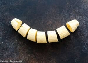 Sliced pieces of peeled plantain arranged in a row on a dark, textured surface—perfect for learning How to Make Tostones (Crispy Fried Green Plantains – Easy & Authentic!).