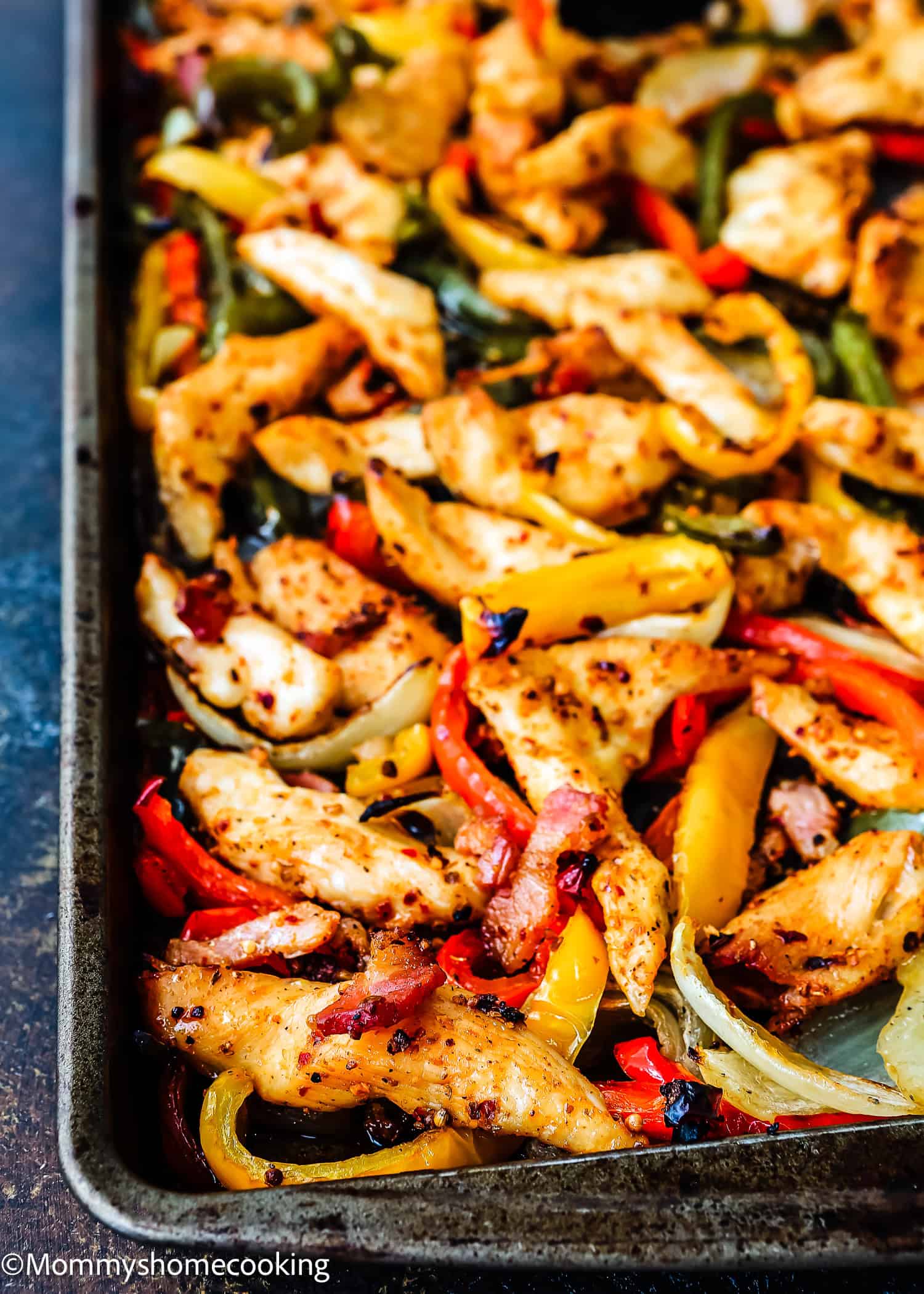 Sheet pan with seasoned, cooked strips of barbecue bacon chicken fajitas, red and yellow bell peppers, and onions.