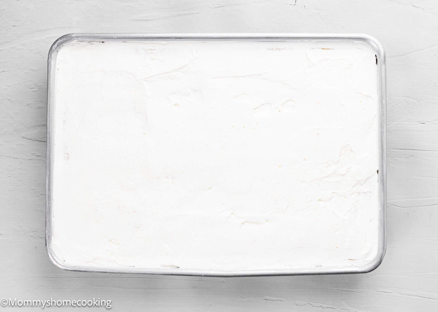 Rectangular metal baking pan filled with a smooth, white frosted dessert, placed on a light-colored surface—the Best Eggless Tres Leches Cake.