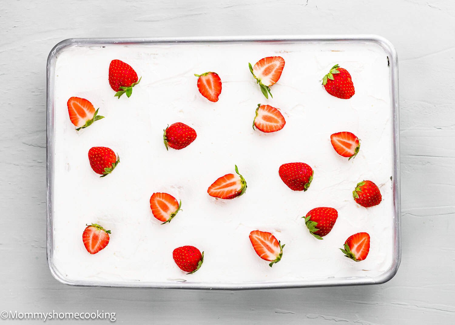 Rectangular cake in a metal pan topped with white frosting and evenly spaced fresh strawberries, some whole and some halved. The Best Eggless Tres Leches Cake offers a delightful treat for any occasion.