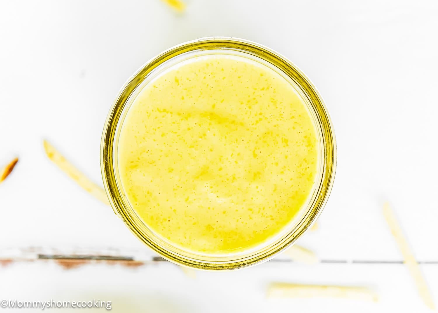A glass filled with a thick, yellow smoothie or drink, inspired by The Best Sweet Corn Sauce (Venezuelan-Style & Irresistibly Creamy), is viewed from above on a white surface.