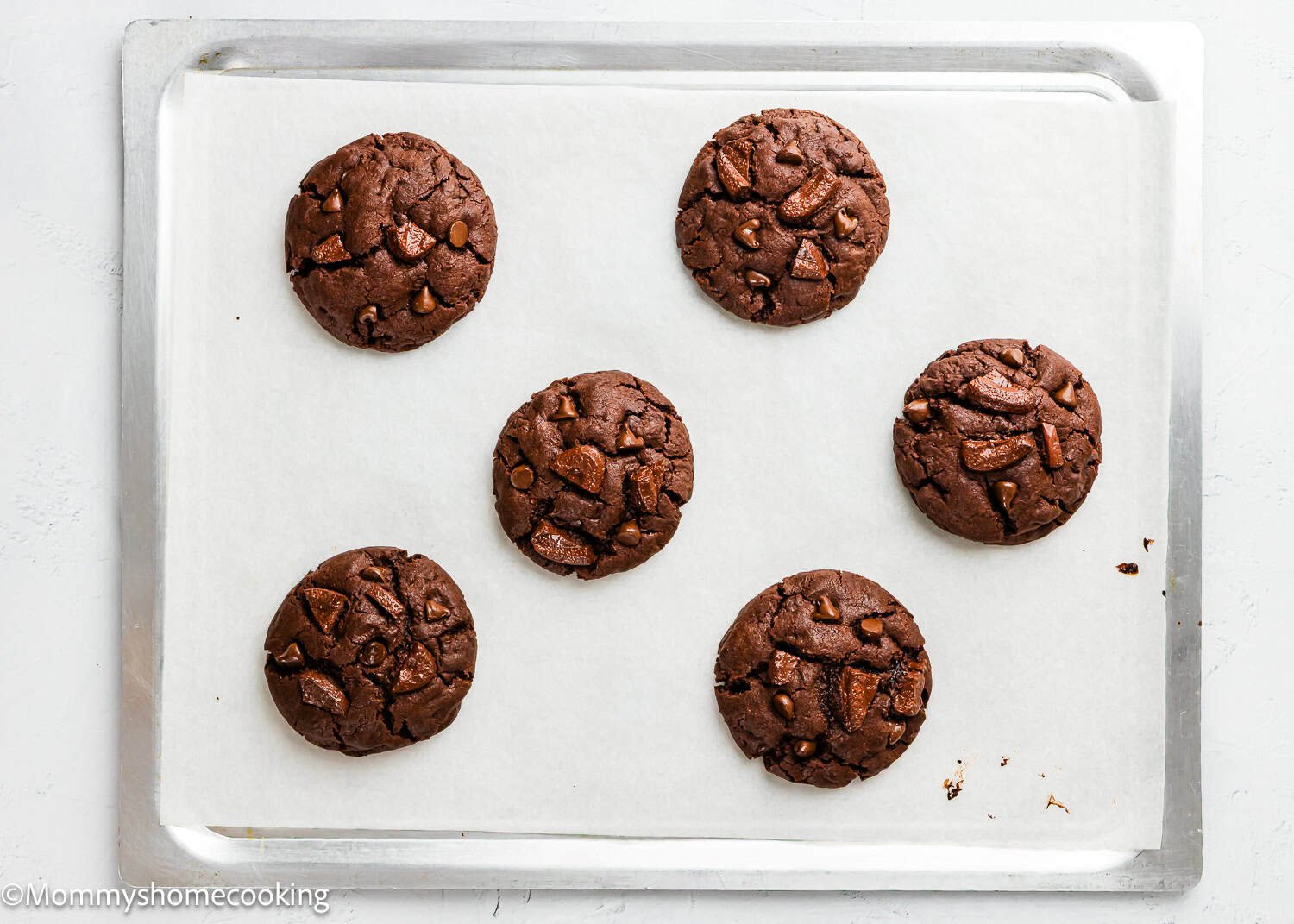 Six Ultimate Chocolate Cookies (Egg-Free) with chocolate chunks are evenly spaced on a parchment-lined baking sheet.