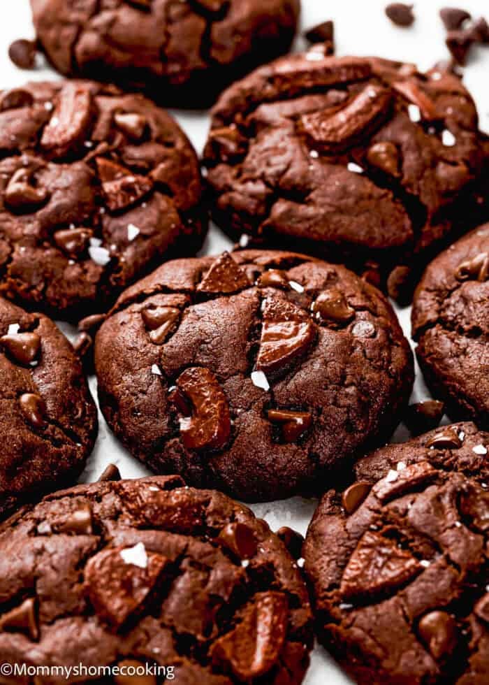 Close-up of several Ultimate Chocolate Cookies (Egg-Free) with chocolate chunks and small sea salt flakes on top.