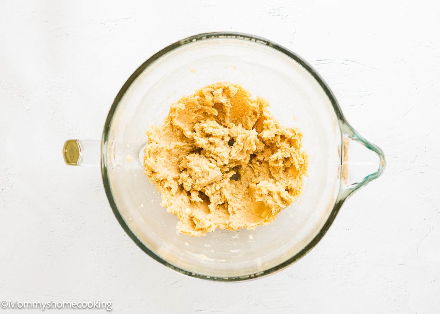 A glass mixing bowl containing creamed Ultimate Chocolate Cookies (Egg-Free) dough mixture on a white surface.