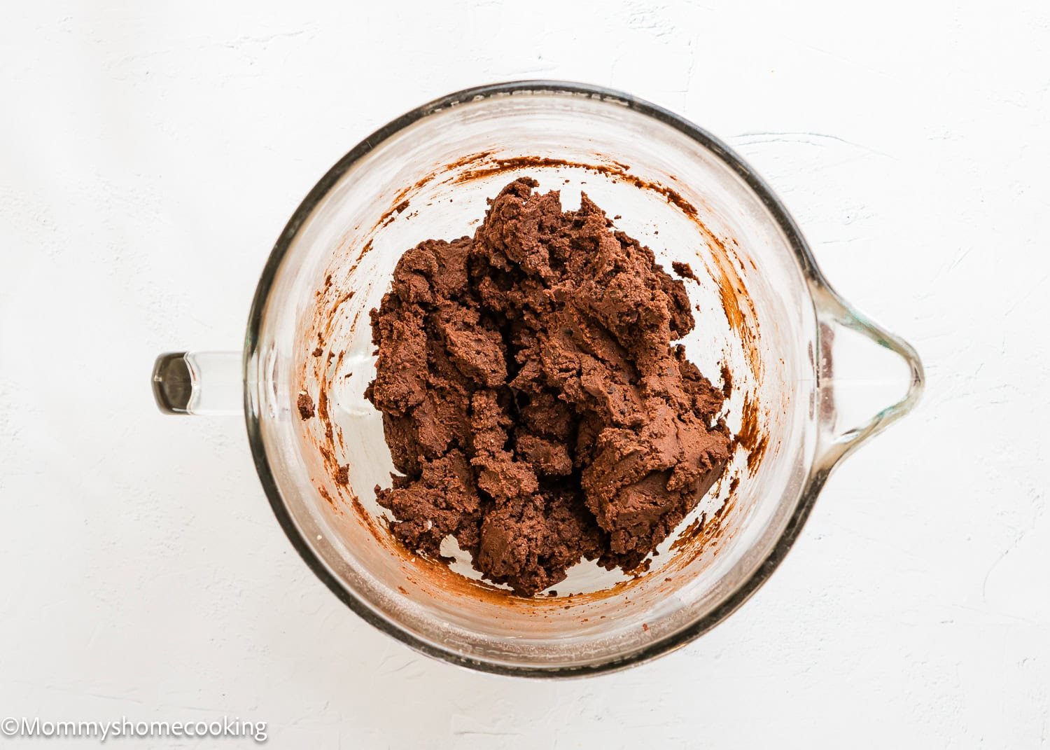 A glass mixing bowl containing a mound of Ultimate Chocolate Cookies (Egg-Free) dough on a white surface.