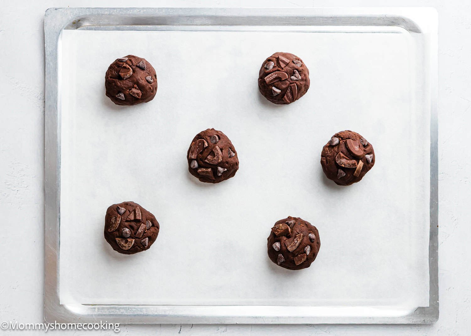 Six unbaked Ultimate Chocolate Cookies (Egg-Free) dough balls with chocolate chunks are arranged on a parchment-lined baking sheet.