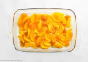 A glass baking dish filled with sliced peaches and syrup arranged evenly on the bottom, perfect for making the Ultimate Easy Peach Dump Cake (5 Ingredients).