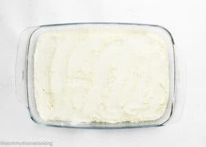 A glass baking dish filled with an even layer of white, powdered ingredients on a white surface—perfect for preparing the Ultimate Easy Peach Dump Cake (5 Ingredients).