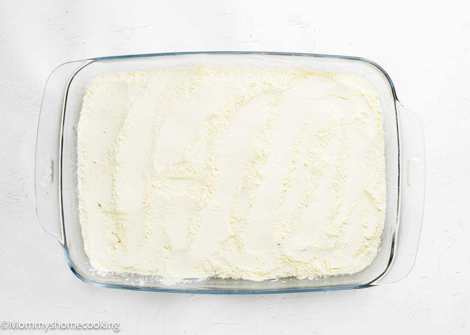 A glass baking dish filled with an even layer of white, powdered ingredients on a white surface—perfect for preparing the Ultimate Easy Peach Dump Cake (5 Ingredients).