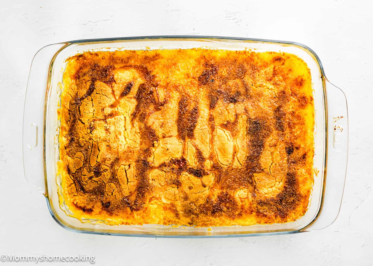 A rectangular glass baking dish filled with golden-brown Ultimate Easy Peach Dump Cake (5 Ingredients) on a white surface.